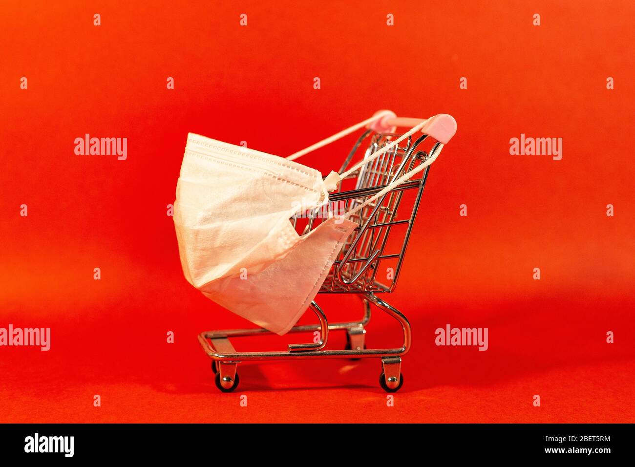 Carrello con maschera medica protettiva contro il coronavirus. Shopping sicuro e online sul concetto di quarantena. Sfondo rosso. Foto Stock