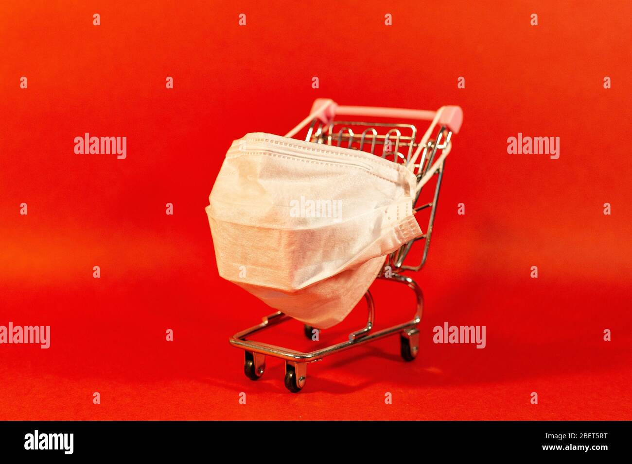 Carrello con maschera medica protettiva contro il coronavirus. Shopping sicuro e online sul concetto di quarantena. Sfondo rosso. Foto Stock
