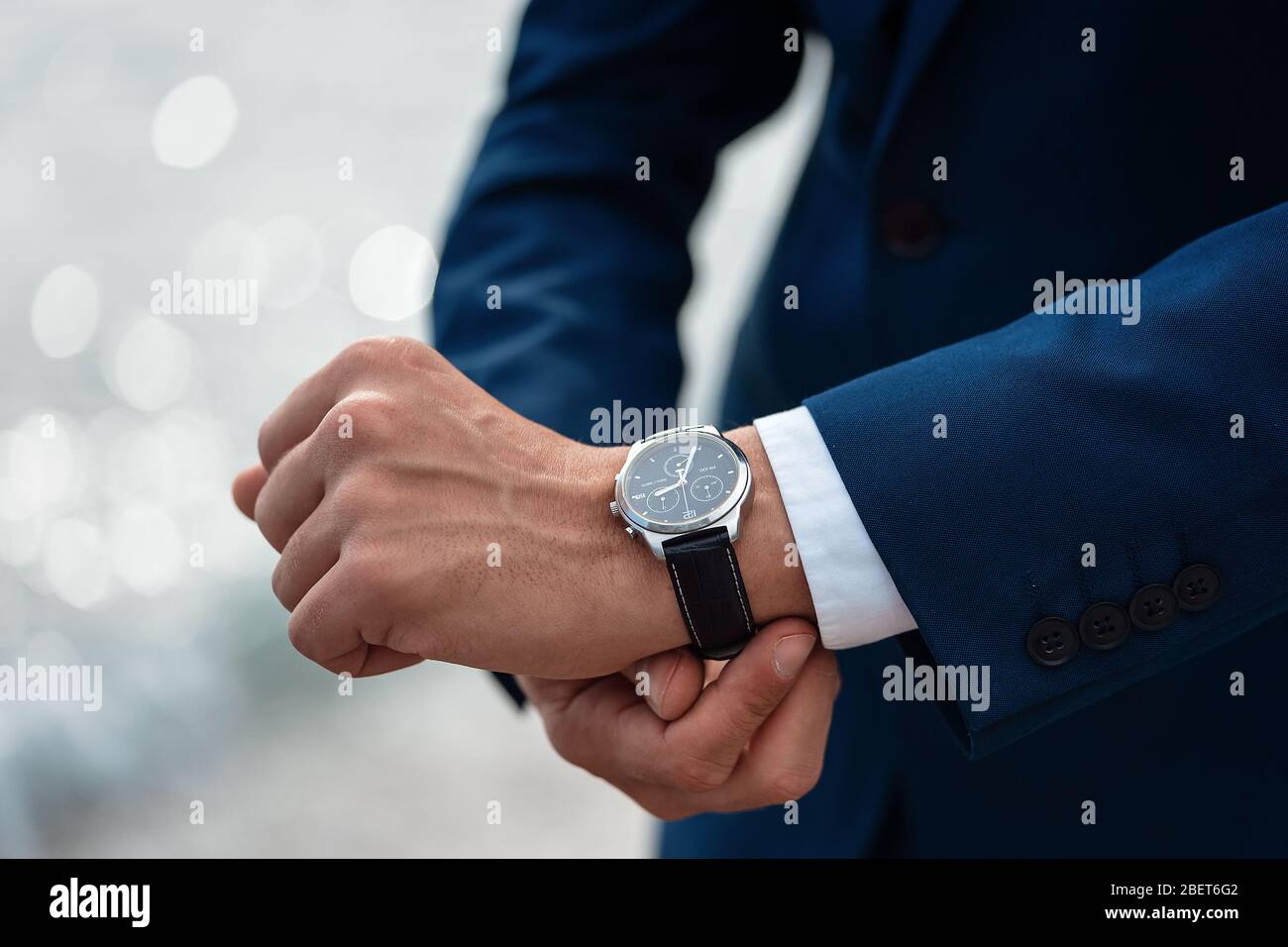 Un uomo in un vestito da lavoro che controlla un orologio da polso sulla sua mano sul mare di fondo Foto stock Alamy