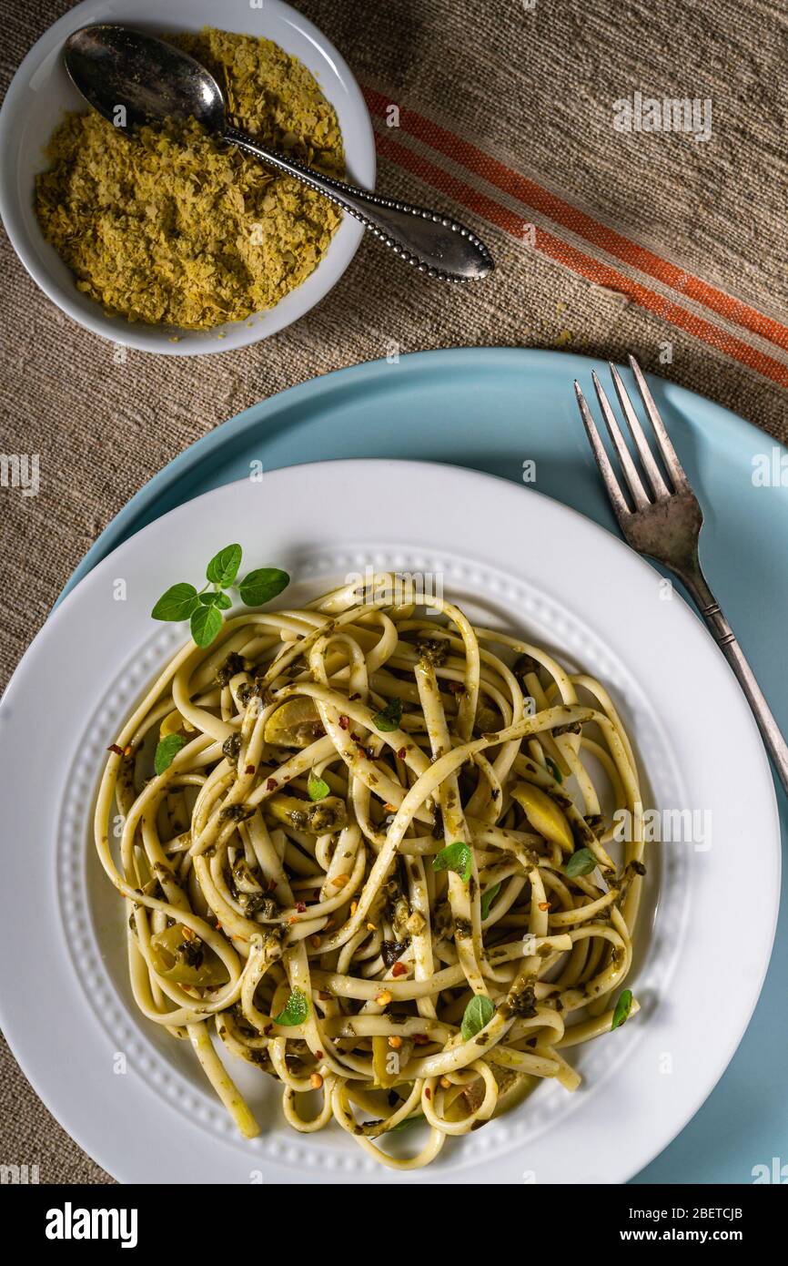 Piatto di pasta vegana. Fettuccine al pesto, olive verdi timo fresco e lievito nutritivo. Foto Stock
