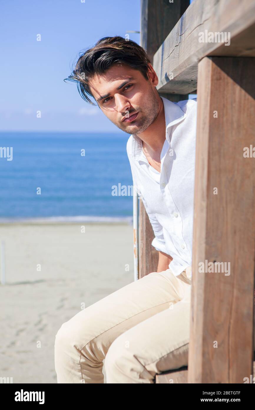 Bell'uomo si rilassò al mare, con vista su una struttura in legno. Mare e  cielo blu. Il giovane indossa una camicia bianca con pantaloni beige, ha  Foto stock - Alamy