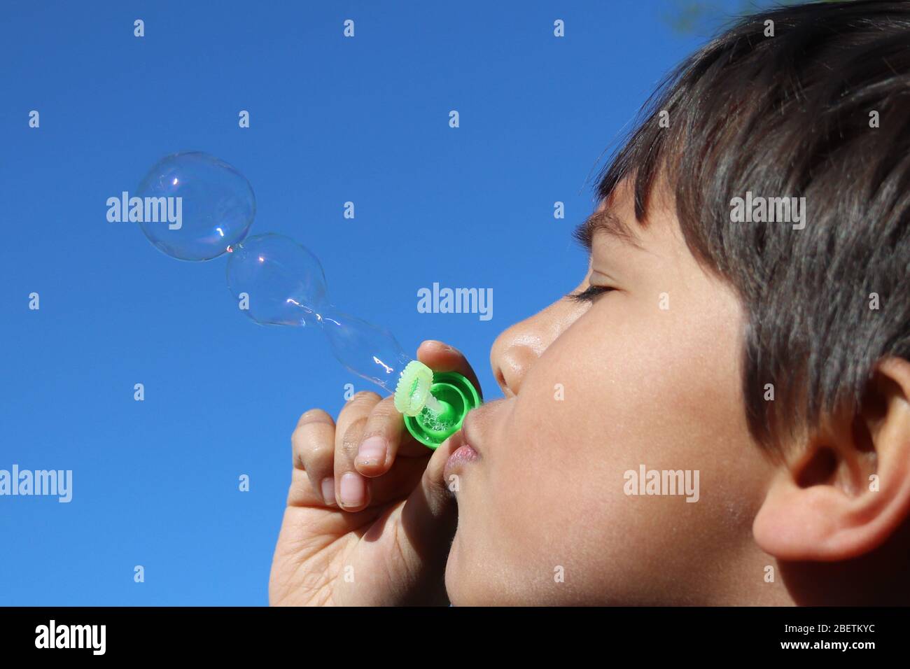 Ragazzo che soffia bolle fuori al sole con cielo blu Foto Stock