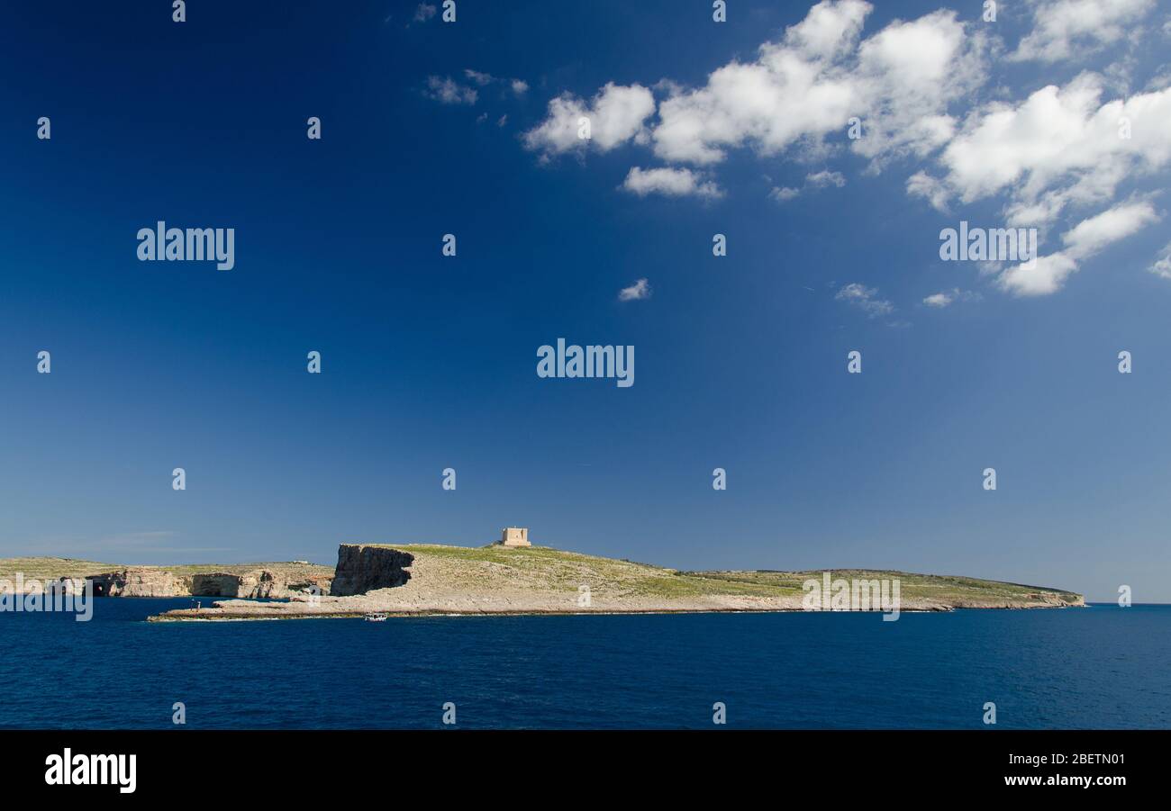 Cielo blu e nuvole bianche sopra la Torre di Santa Maria torre di guardia bascata sull'isola di Comino o KEMUNA dell'Arcipelago Maltese nella Mediterra Foto Stock