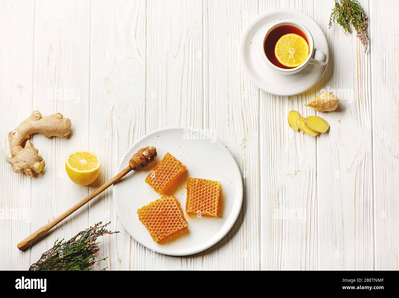 Piatto di nidi d'api con cucchiaio di miele, limone, zenzero e tazza di tè su sfondo di legno bianco con spazio per le copie. Concetto di medecina naturale. Foto Stock