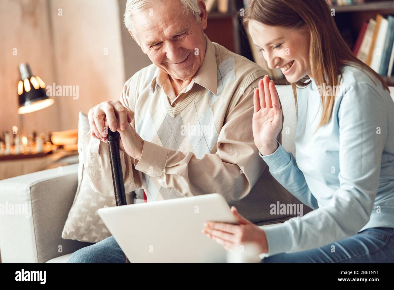 Padre e figlia a casa libreria seduta a guardare video chiamata sul laptop sventolando felice Foto Stock