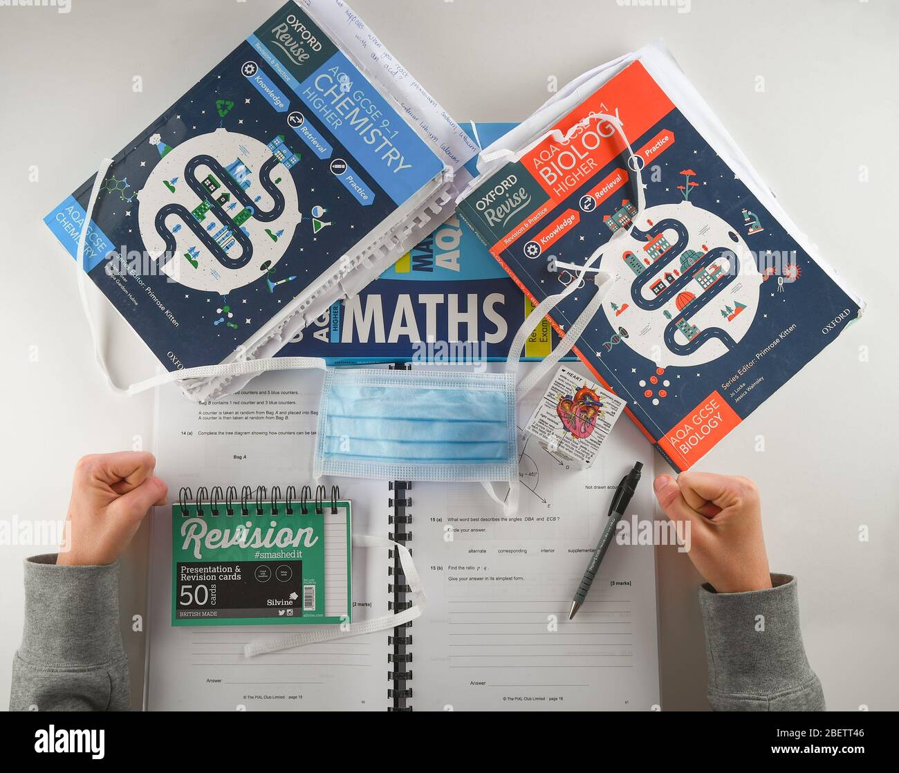 Un'immagine concettuale da utilizzare con gli esami GCSE annullati a causa di coronavirus. Studente con libri di revisione accanto a una maschera facciale PPE. Foto Stock