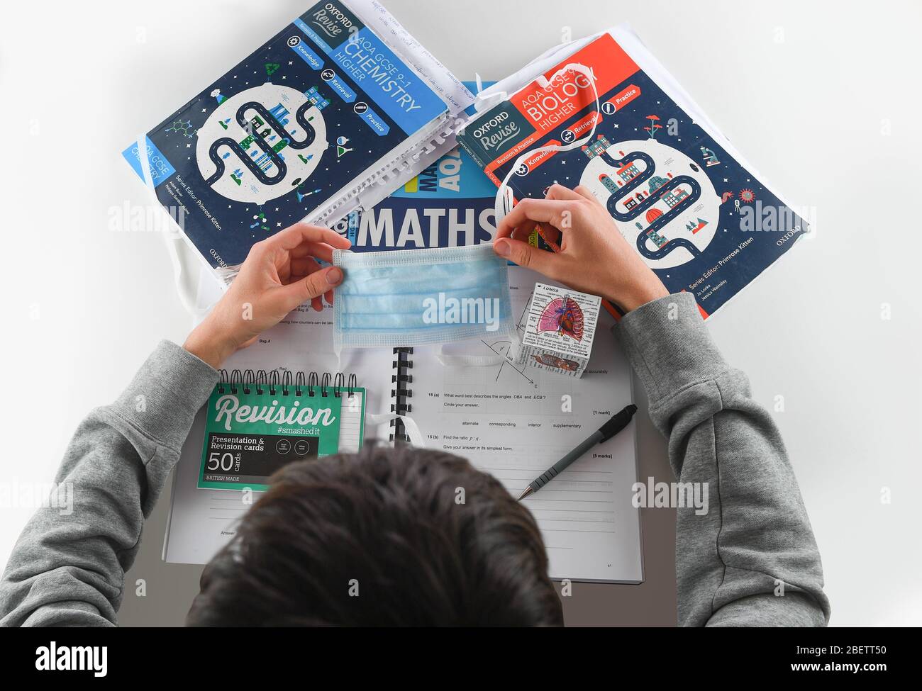 Un'immagine concettuale da utilizzare con gli esami GCSE annullati a causa di coronavirus. Studente con libri di revisione accanto a una maschera facciale PPE. Foto Stock
