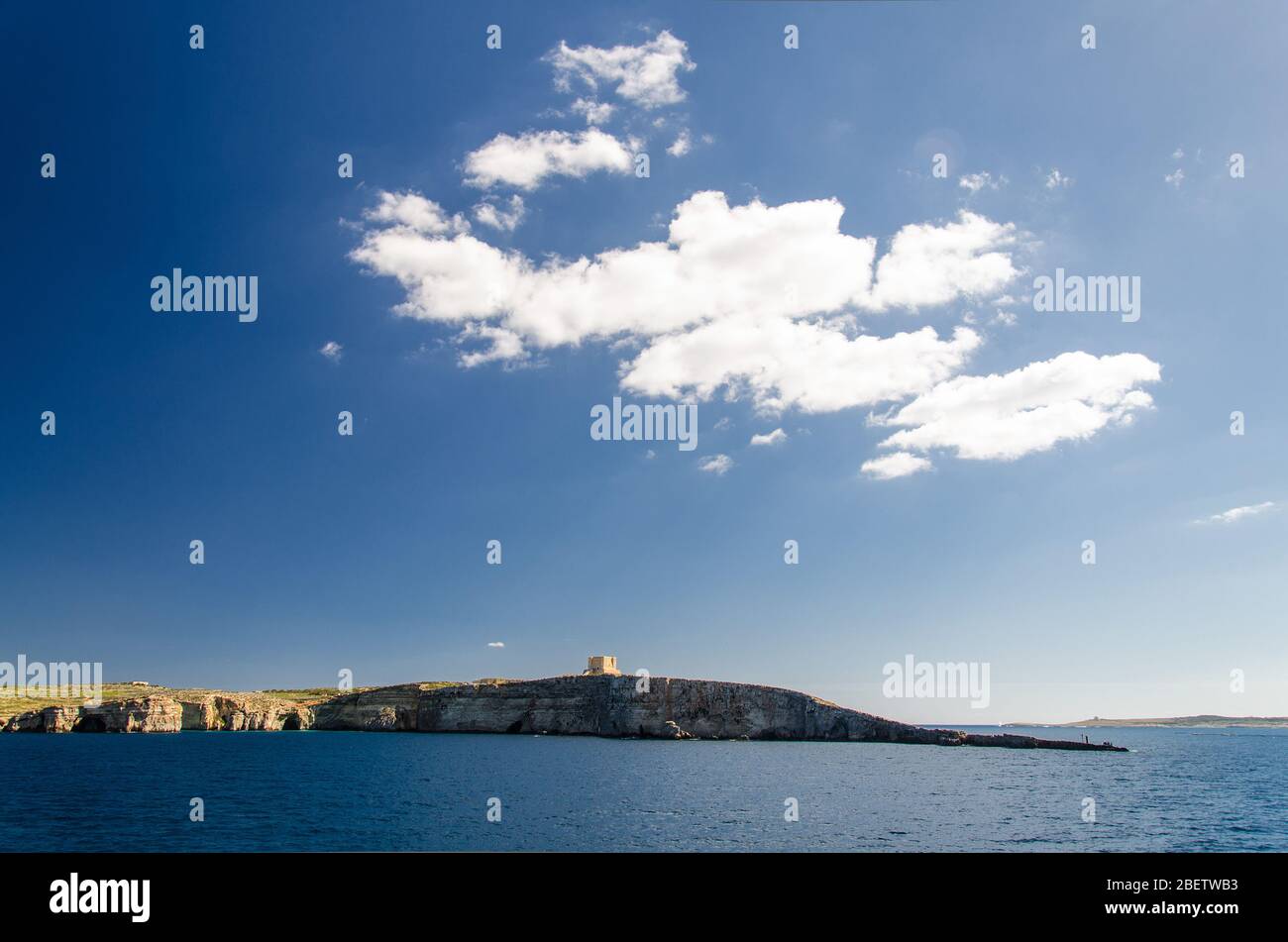 Cielo blu e nuvole bianche sopra la Torre di Santa Maria torre di guardia bascata sull'isola di Comino o KEMUNA dell'Arcipelago Maltese nella Mediterra Foto Stock