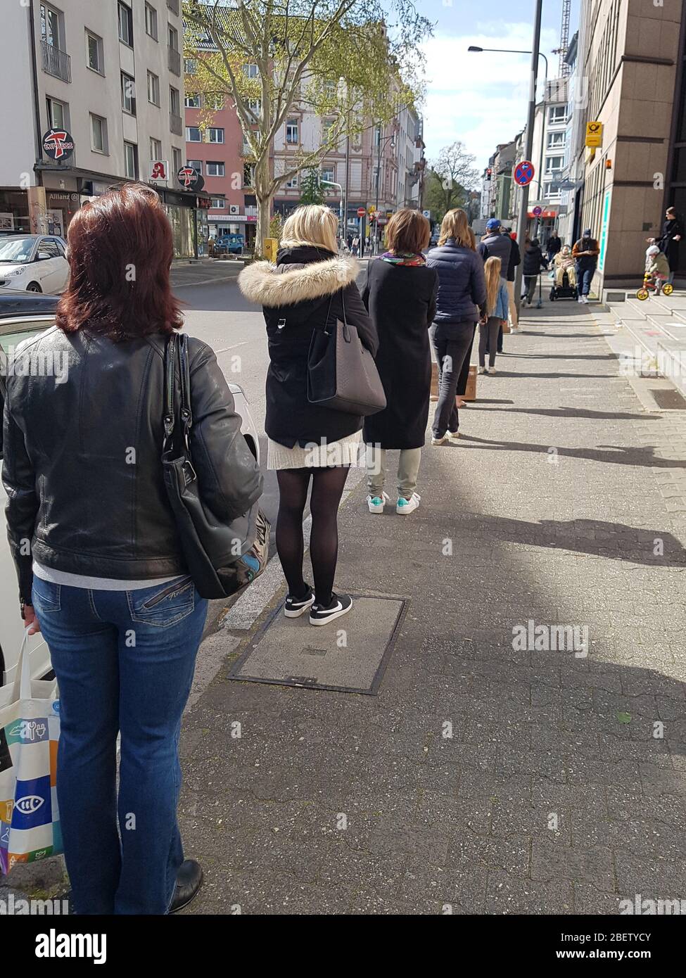 Coda o coda di attesa di persone all'ingresso dell'ufficio postale e del supermercato con 1.5 metri di distanza di sicurezza / sei piedi di separazione - corona virus covid-19 Foto Stock