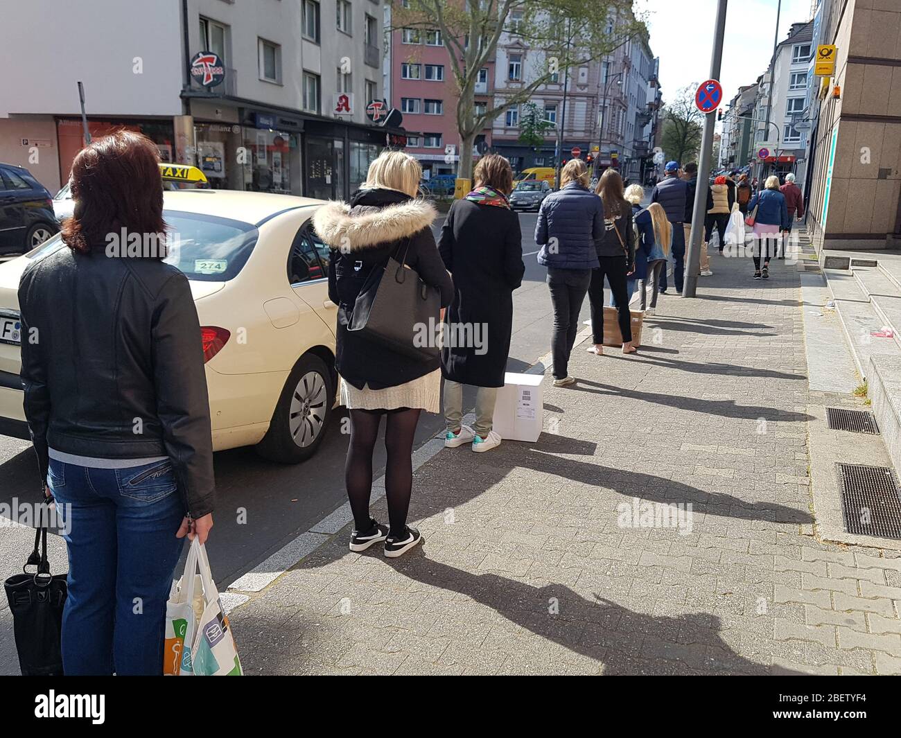 Coda o coda di attesa di persone all'ingresso dell'ufficio postale e del supermercato con 1.5 metri di distanza di sicurezza / sei piedi di separazione - corona virus covid-19 Foto Stock