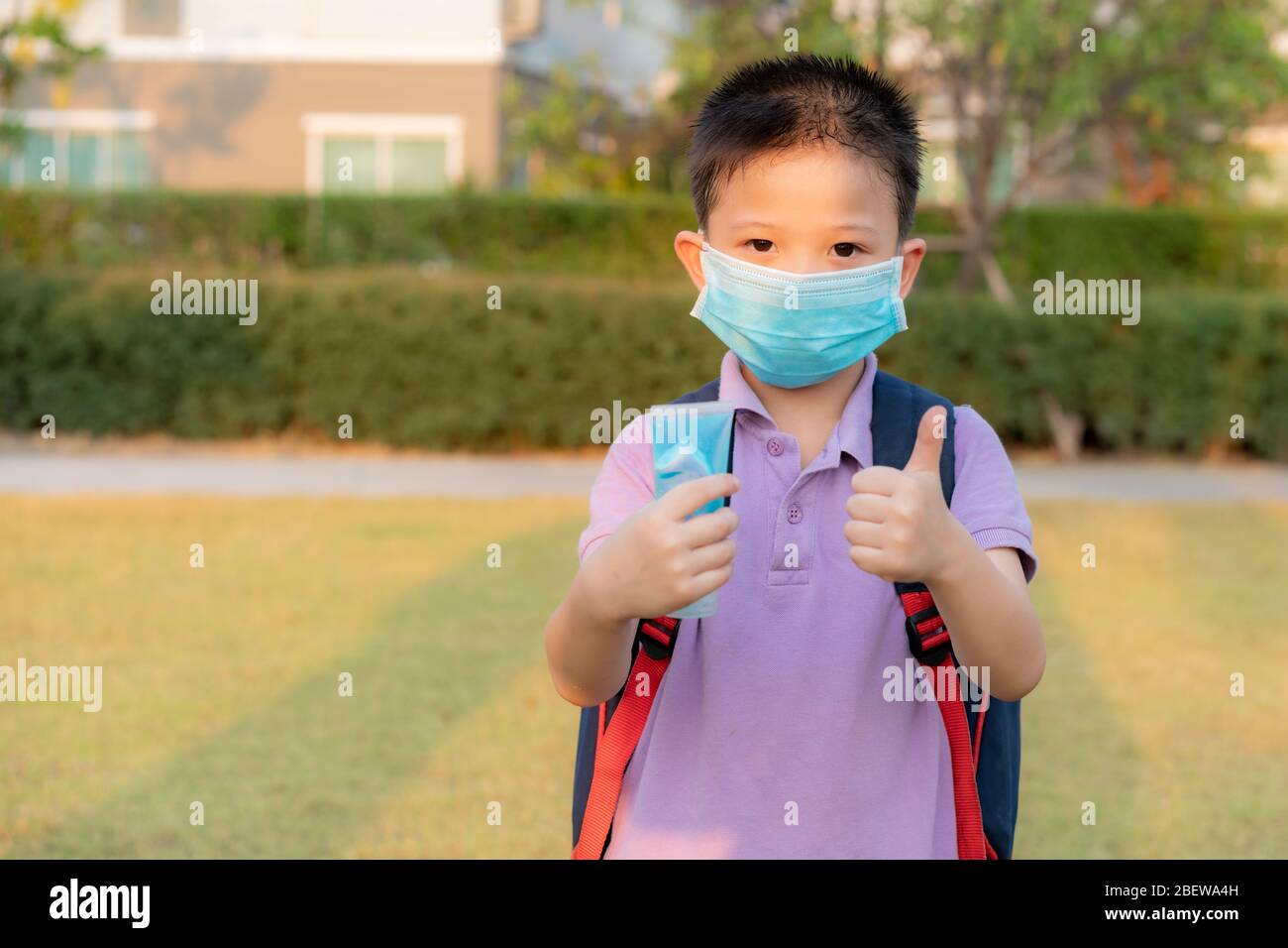 Bambino asiatico che indossa maschera protettiva con alcol gel antisettico e pollice su, prevenzione, pulizia delle mani frequentemente, prevenire infezioni, scoppio Foto Stock