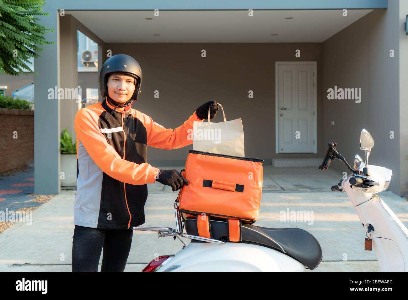 Consegna Asian uomo con uniforme arancione e pronto a spedire consegna di Food bag davanti al cliente con scatola su scooter, cibo espresso deli Foto Stock