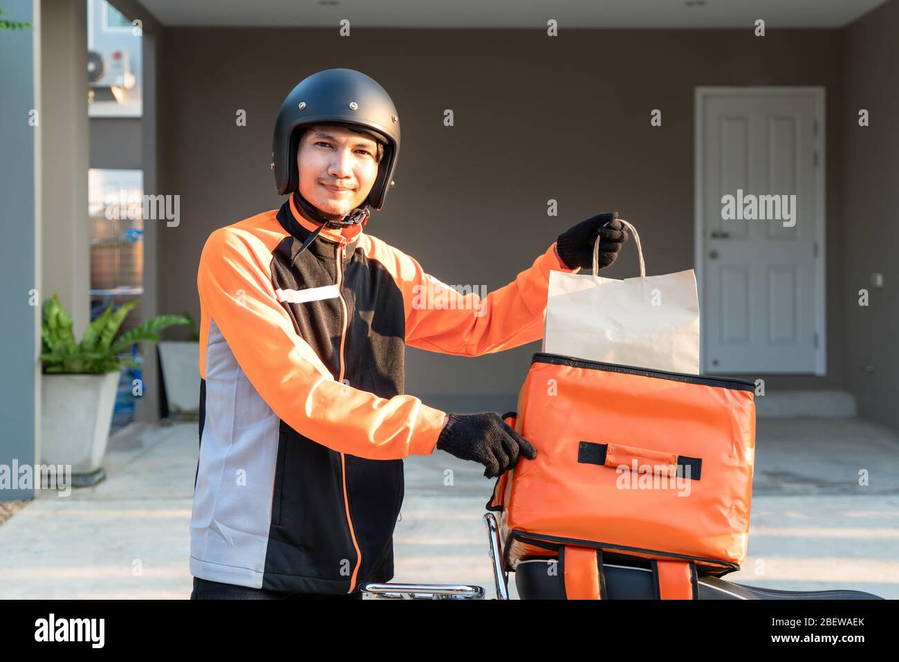 Consegna Asian uomo con uniforme arancione e pronto a spedire consegna di Food bag davanti al cliente con scatola su scooter, cibo espresso deli Foto Stock