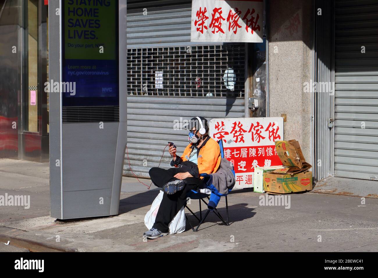 Una persona che indossa un respiratore industriale si rilassa su un marciapiede di New York guardando i video durante il... PER ULTERIORI INFORMAZIONI, VEDERE LA DIDASCALIA COMPLETA Foto Stock
