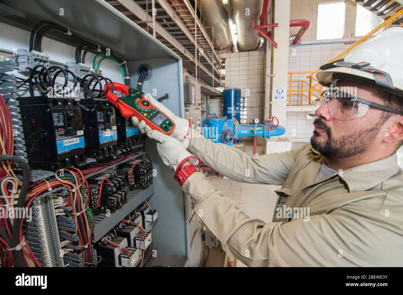 Tecnico elettrico messicano che esegue la manutenzione ad un pannello di controllo elettrico del motore nel settore geotermico. Apprendista di lavori qualificati. Foto Stock