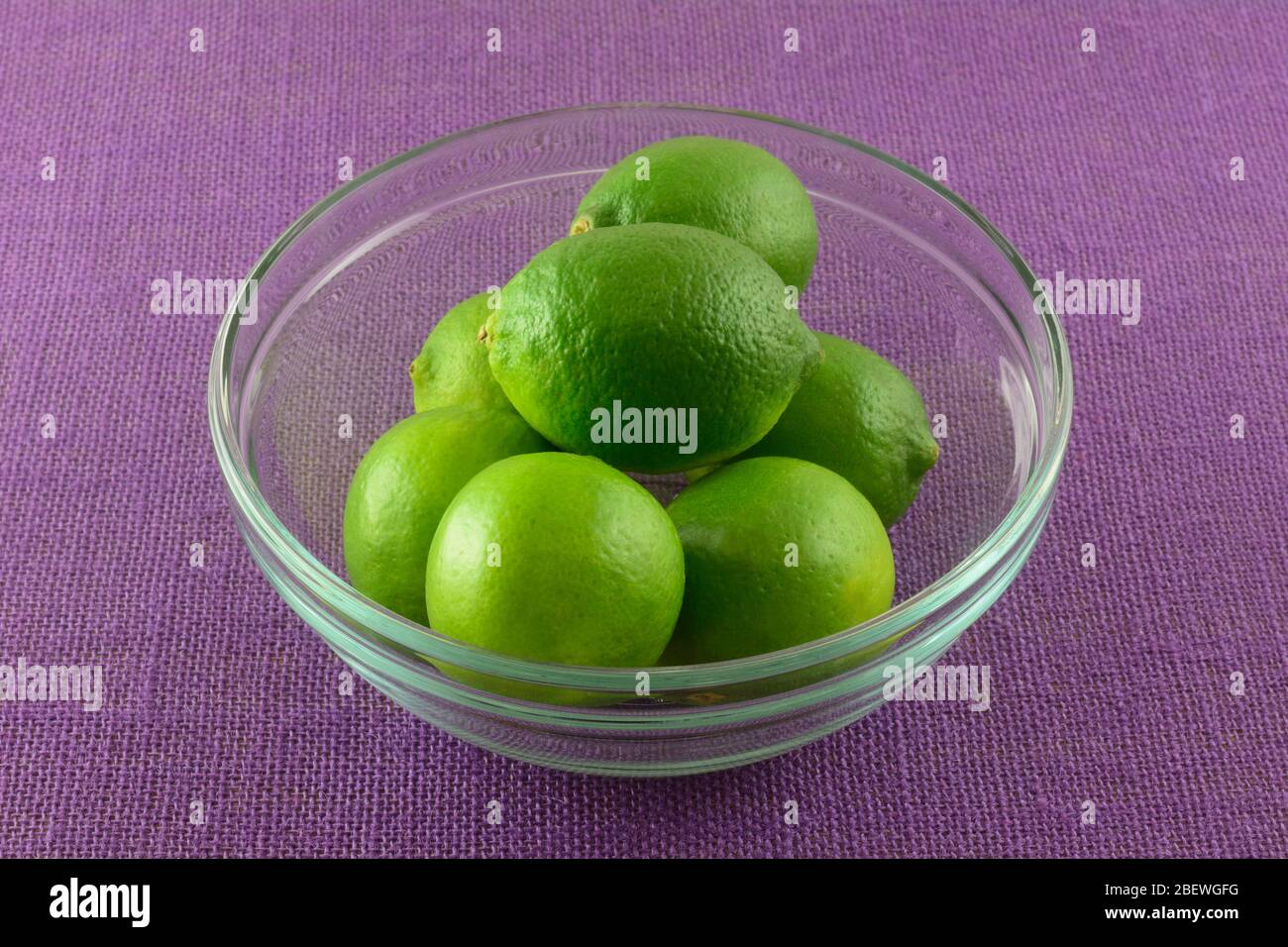 Lime crude fresche in ciotola di frutta di vetro su tovaglia viola Foto Stock