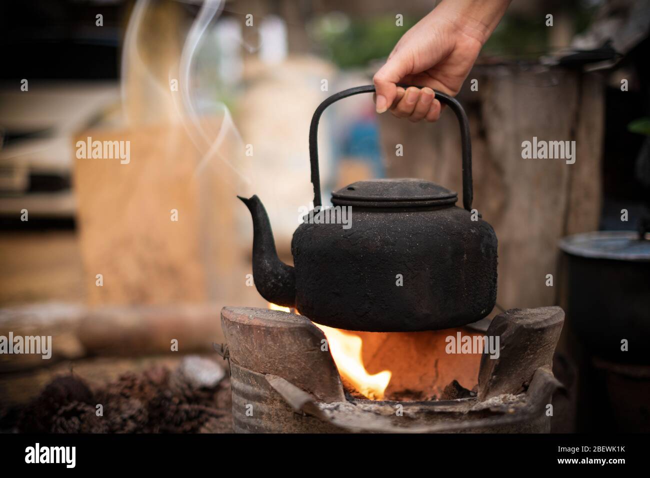 Chiudi mano tenendo bollire acqua vecchio bollitore sul fuoco con una stufa a carbone su sfondo sfocato Foto Stock