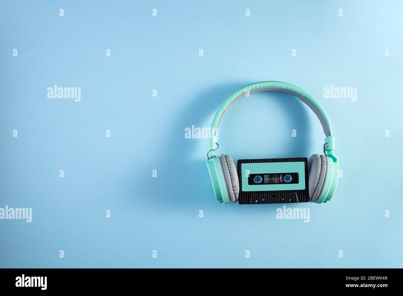 Cuffie turchesi con cassetta audio su sfondo blu. Concetto musicale con copyspace. Foto Stock
