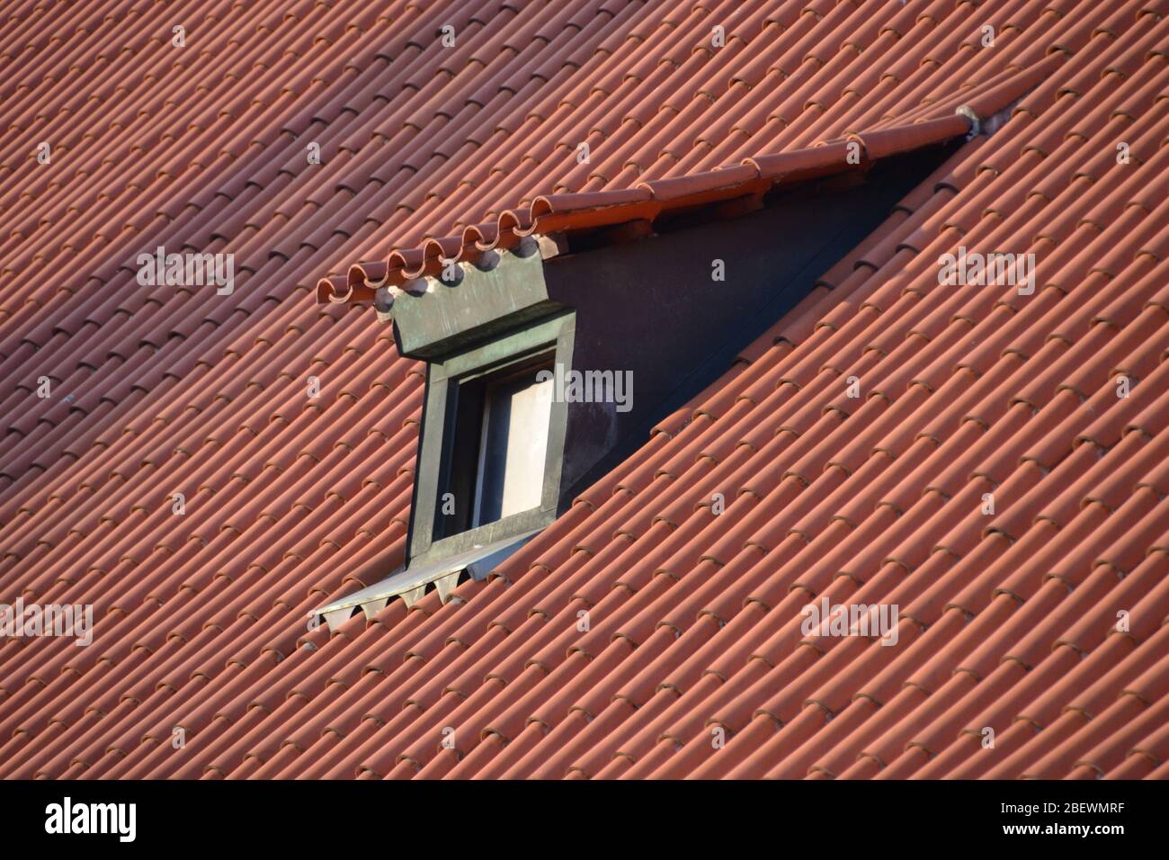 Piccola finestra verde dormer in un mare di piastrelle rosse sul tetto di un edificio a Praga al sole d'inverno Foto Stock