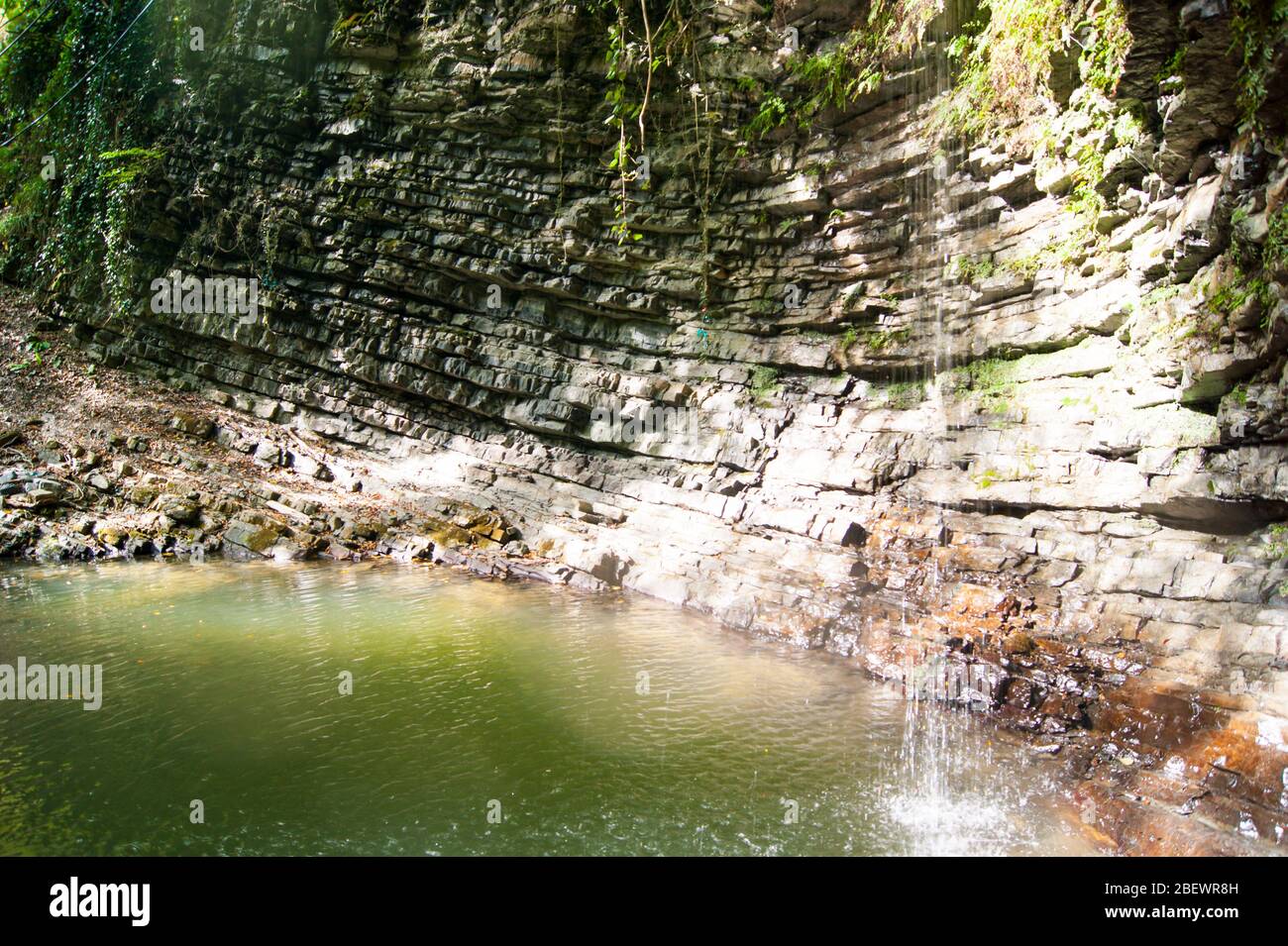 Una piccola cascata di montagna con acqua ghiacciata molto pulita. Gola. Roccia, pietra, acqua, edera. Caucaso, estate, escursione, turismo, vacanze, vacanze, viaggi Foto Stock