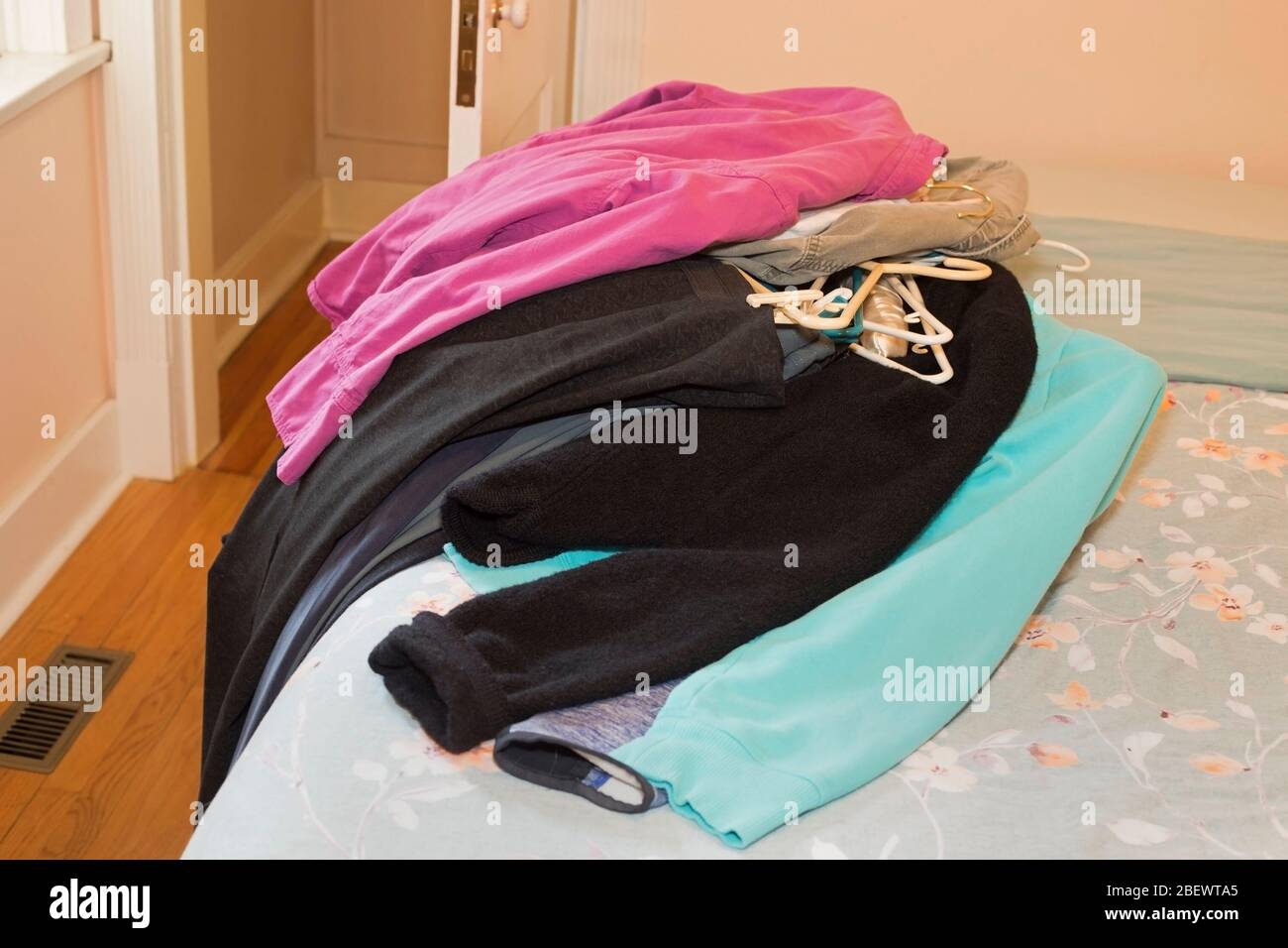 Mucchio di vestiti di donna da ordinare sul letto di fronte a armadio vuoto Foto Stock
