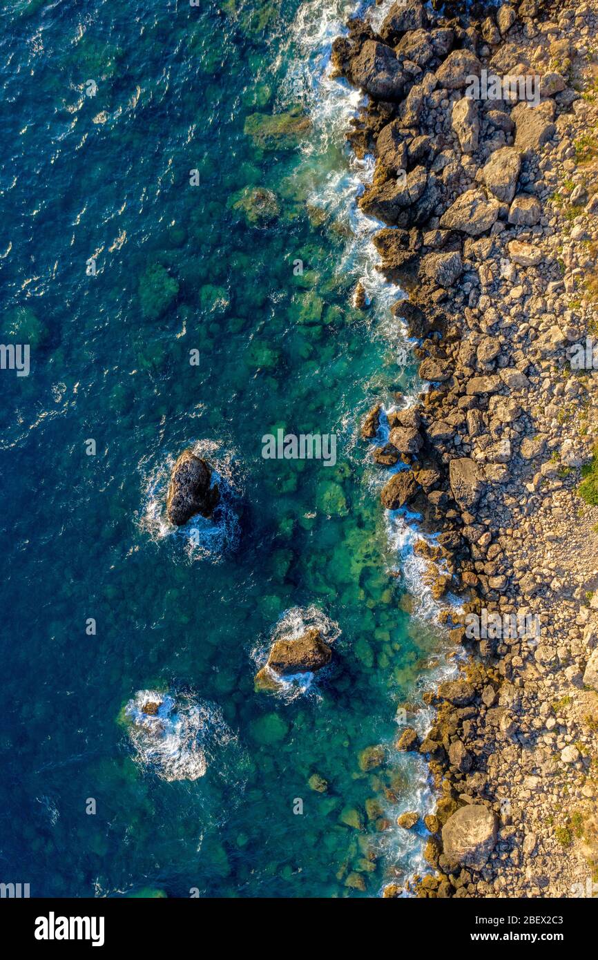 Antenna di onde oceaniche che colpiscono la costa rocciosa. Acqua di mare e rocce di colore torchese sparato dall'aria. Condimento da un drone Foto Stock
