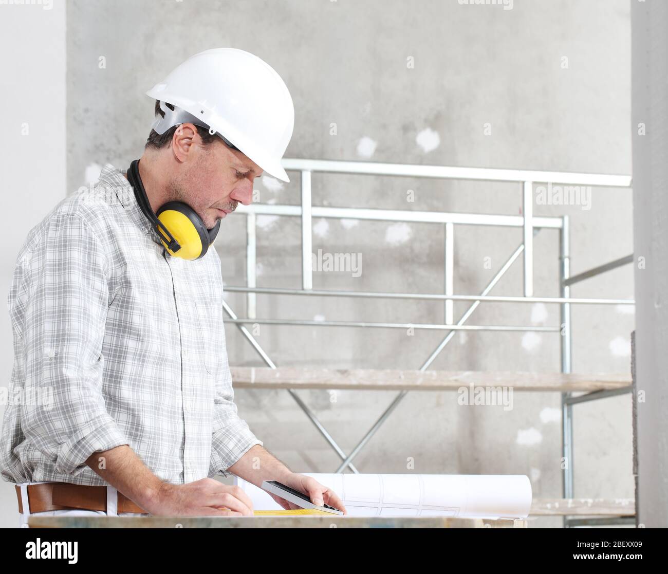 uomo lavoratore di costruzione prende le misure del progetto in cantiere interno Foto Stock