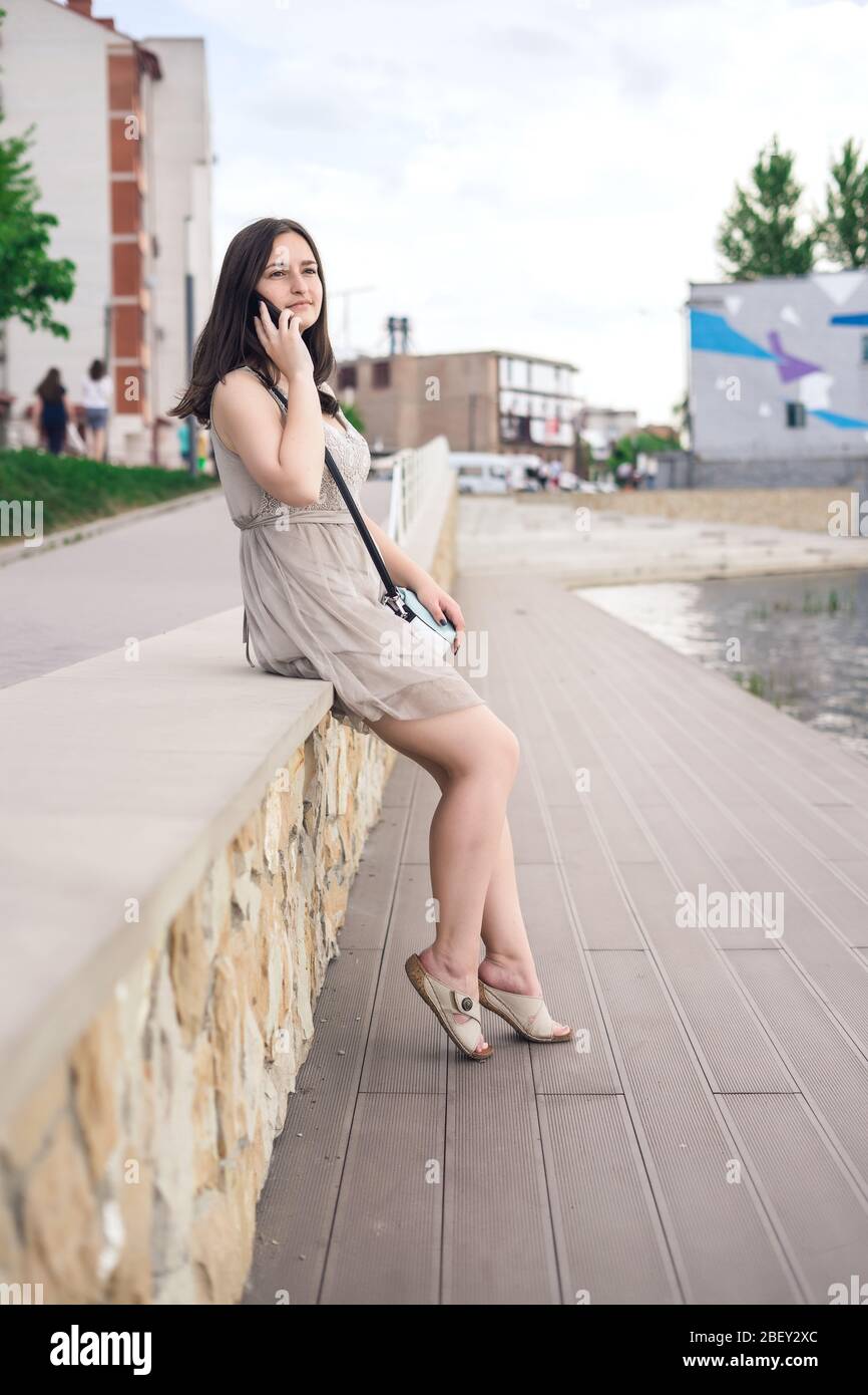 La ragazza parla per telefono sul lungomare. Ragazza in città in una giornata estiva Foto Stock