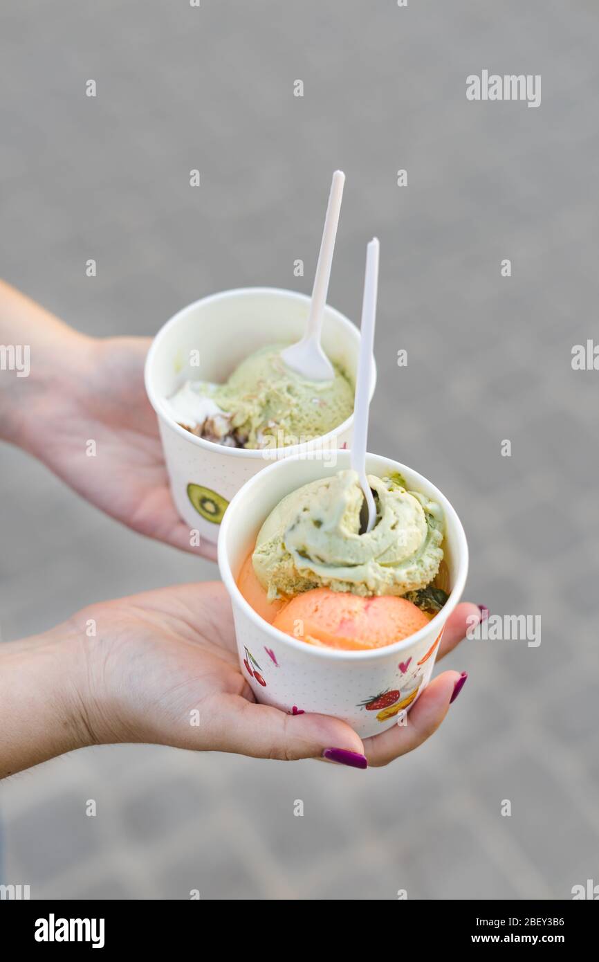 Le mani delle donne tengono una tazza di carta con gelato. Gelato pistacchi e mango Foto Stock