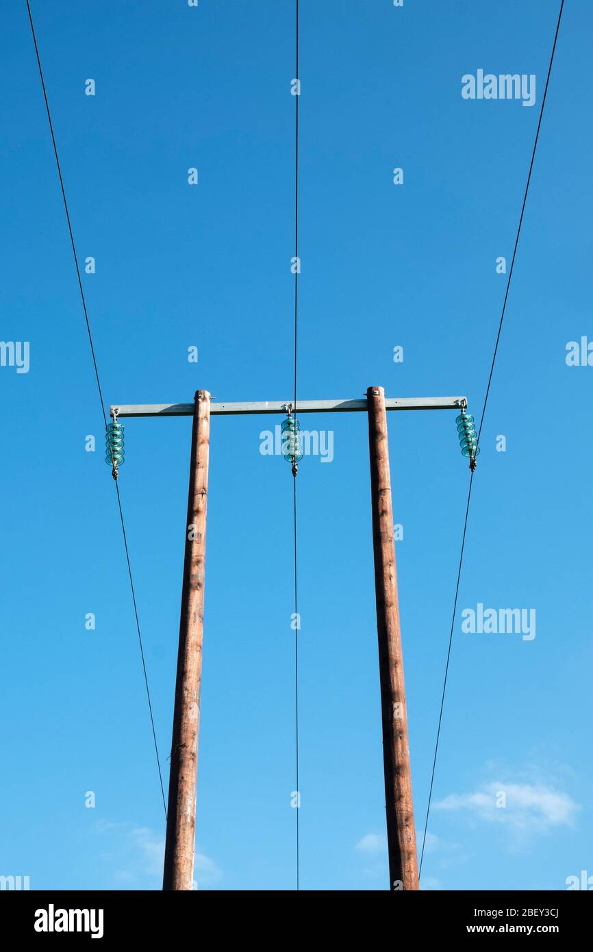 Un palo elettrico in legno ad alta tensione con isolatori in vetro visti contro un cielo blu, nella campagna del Regno Unito Foto Stock
