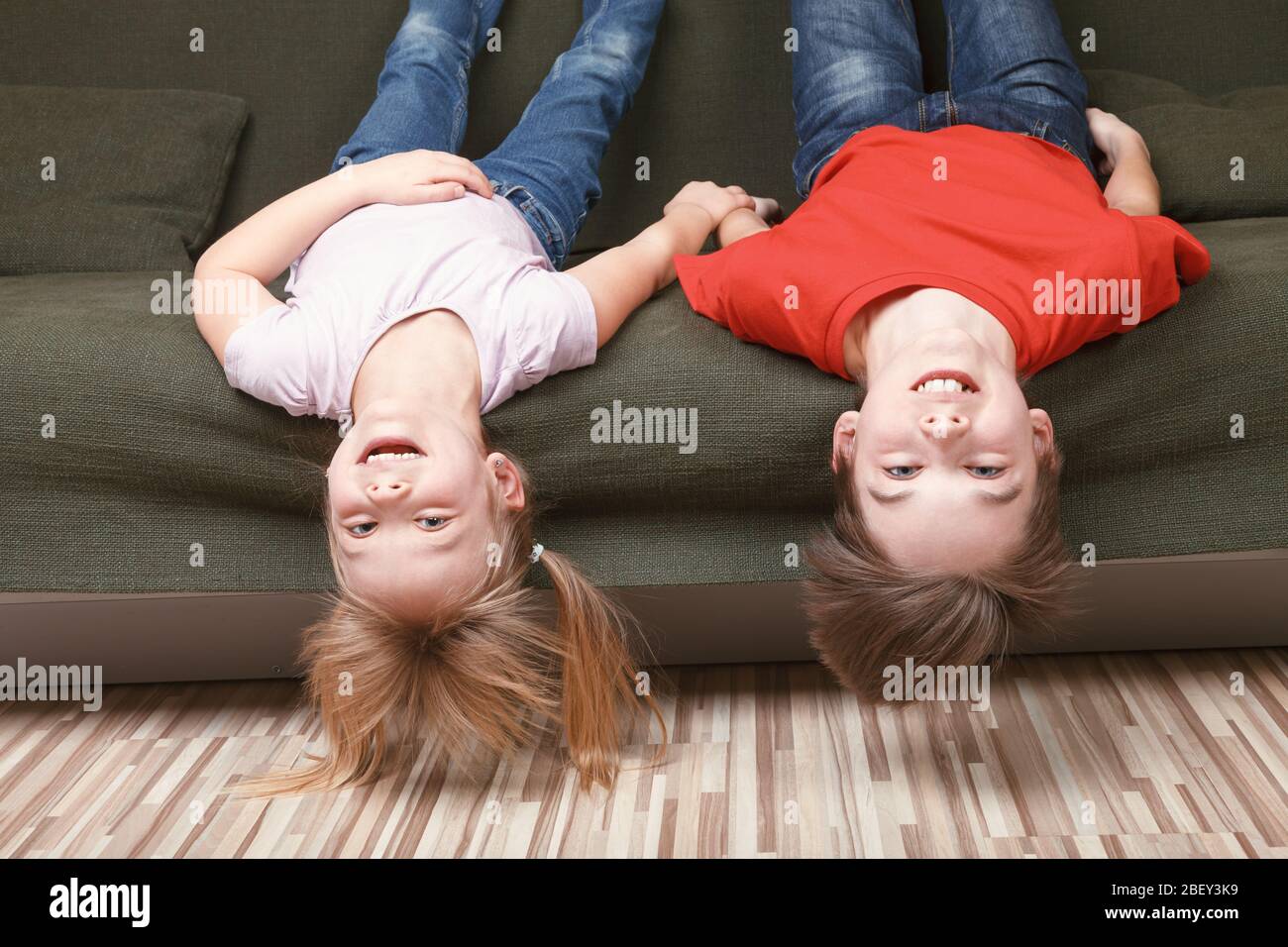 Fratelli felici che si posano sul divano godendosi stare insieme a casa durante l'isolamento di fronte con misure protettive contro la diffusione di coronaviru Foto Stock