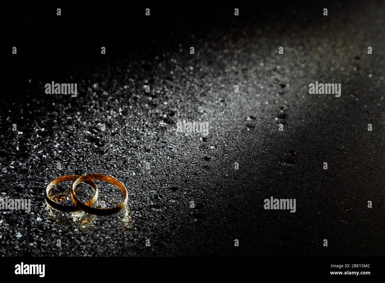 Due anelli di nozze d'oro come simbolo della famiglia. Gli anelli giacciono uno sopra l'altro illuminati da un percorso di luce. Foto Stock