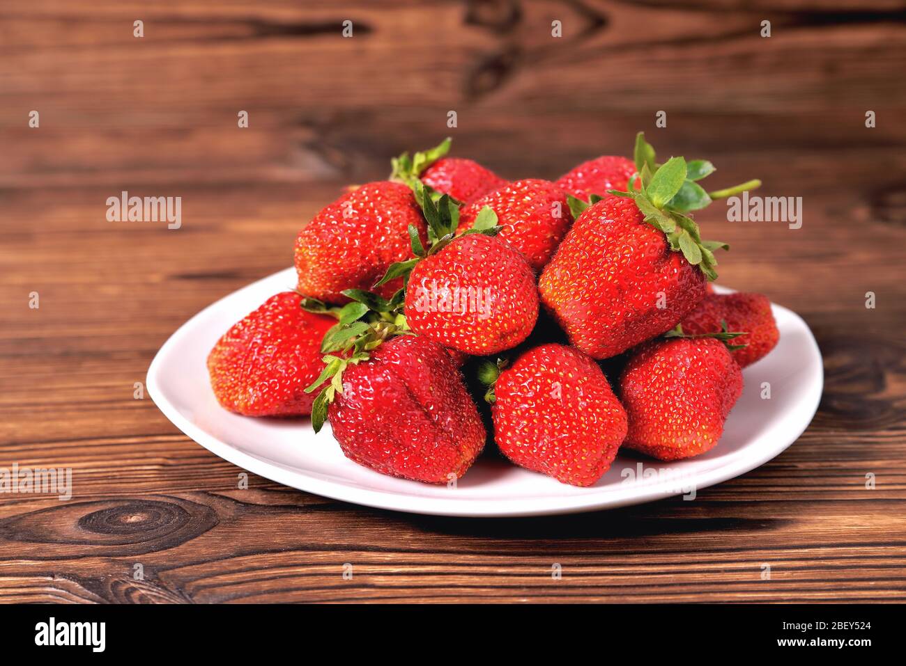 grandi fragole rosse in un piatto bianco su fondo marrone naturale primo piano Foto Stock