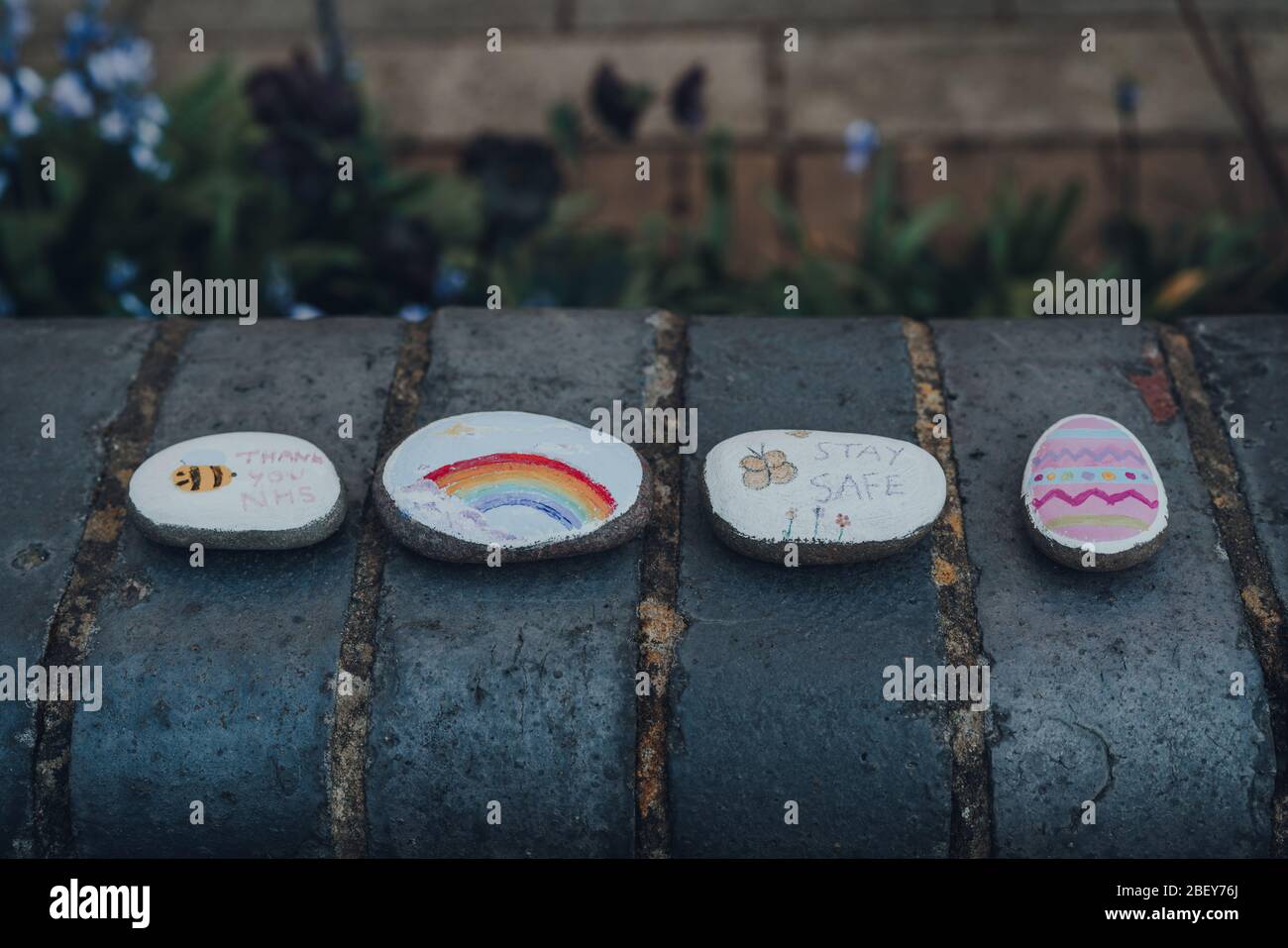 Londra, UK - 12 aprile 2020: Ciottoli dipinti con arcobaleno, uovo di Pasqua, stare al sicuro e grazie messaggi NHS lasciato sulla strada come la gente sostiene ciascuno Foto Stock