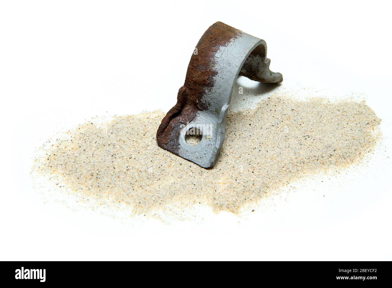 La parte di ghisa arrugginita in parte sabbiata insieme con sabbia isolata su sfondo bianco. Foto Stock