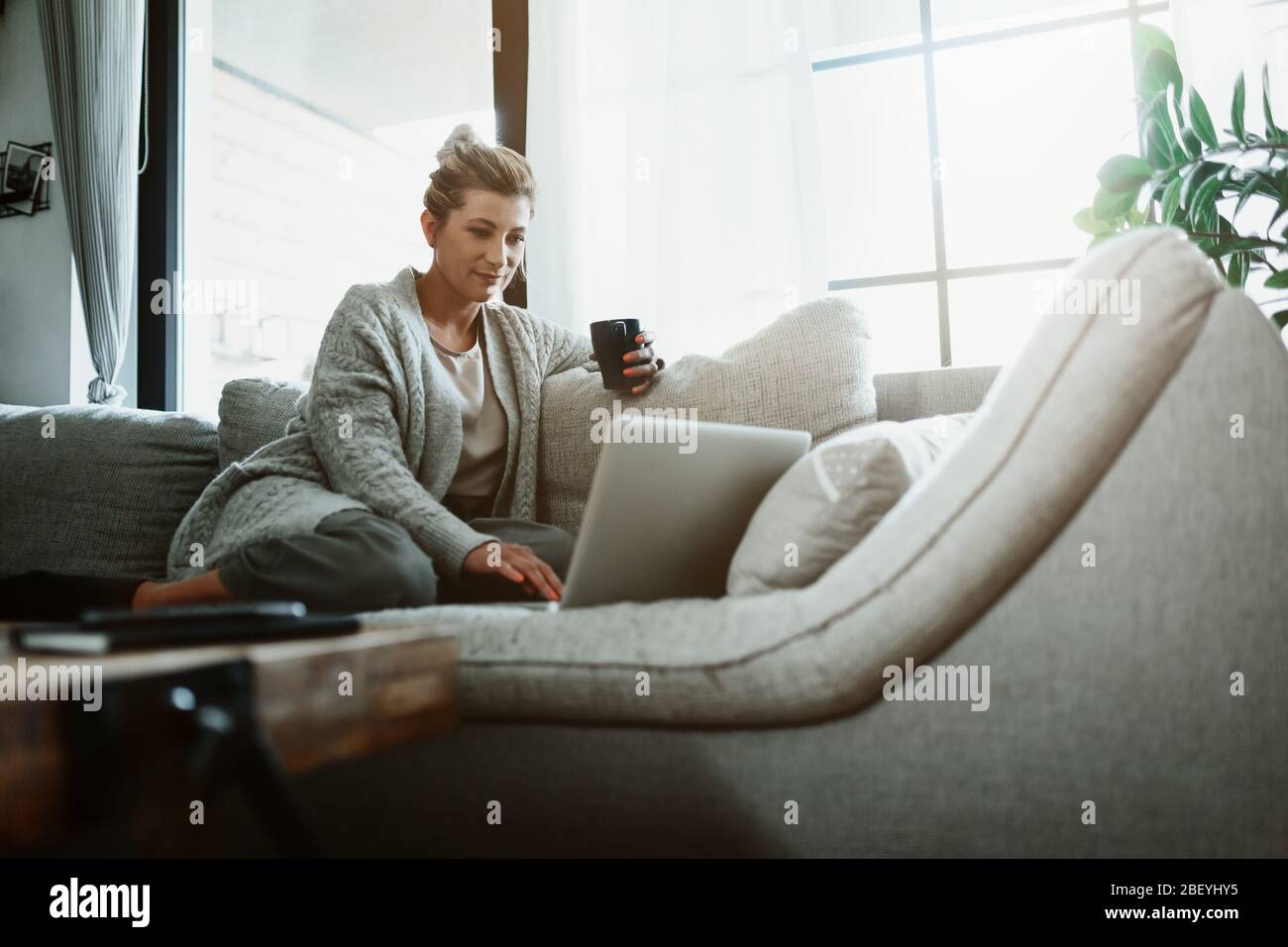Donna d'affari che lavora su un computer portatile seduto a casa e che gestisce la sua attività tramite ufficio domestico durante la quarantena di Coronavirus o Covid-19 Foto Stock