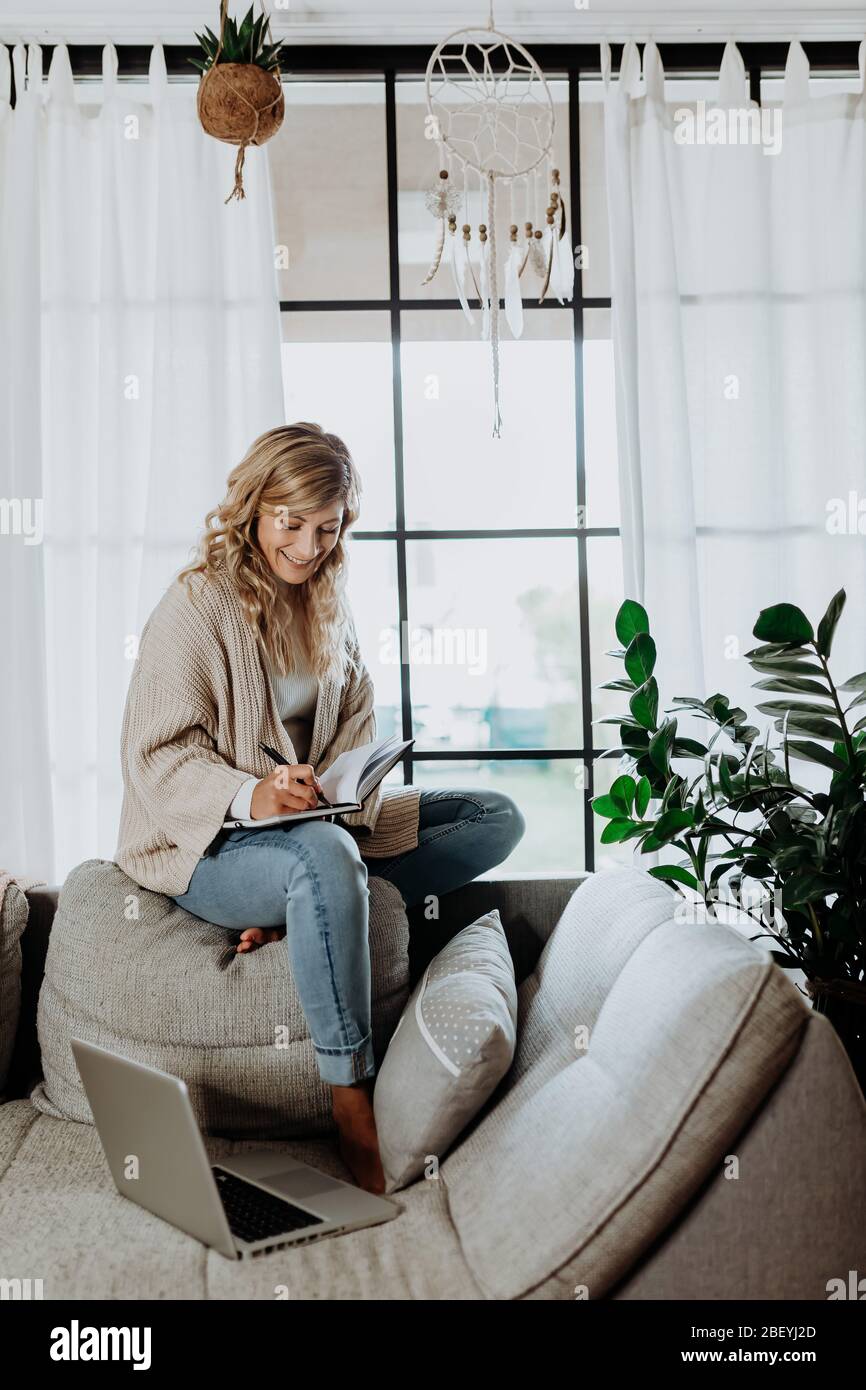 Donna d'affari che lavora su un computer portatile seduto a casa e che gestisce la sua attività tramite ufficio domestico durante la quarantena di Coronavirus o Covid-19 Foto Stock
