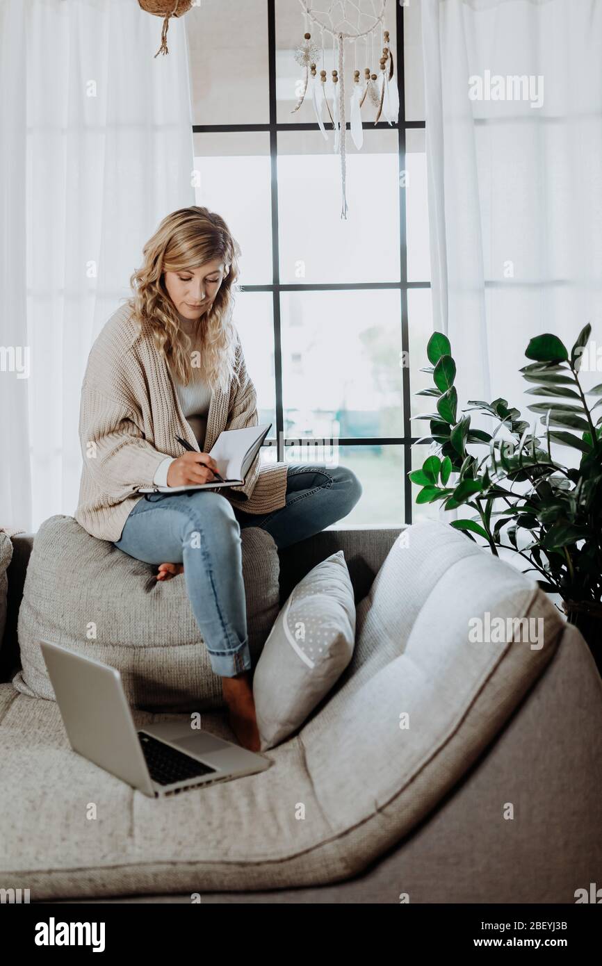 Donna d'affari che lavora su un computer portatile seduto a casa e che gestisce la sua attività tramite ufficio domestico durante la quarantena di Coronavirus o Covid-19 Foto Stock