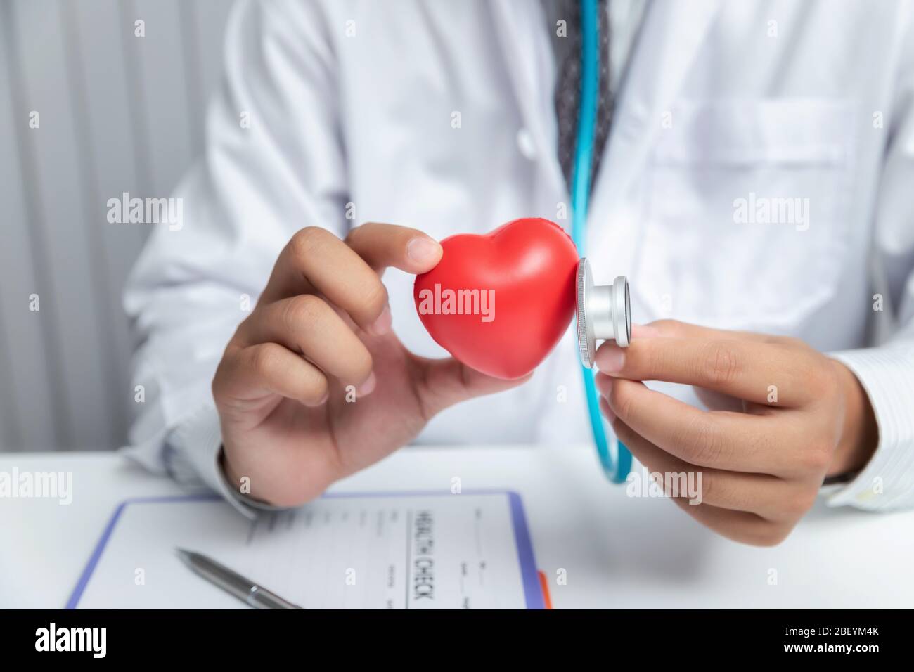 Medico che esamina una palla a forma di cuore rosso con uno stetoscopio. Foto Stock