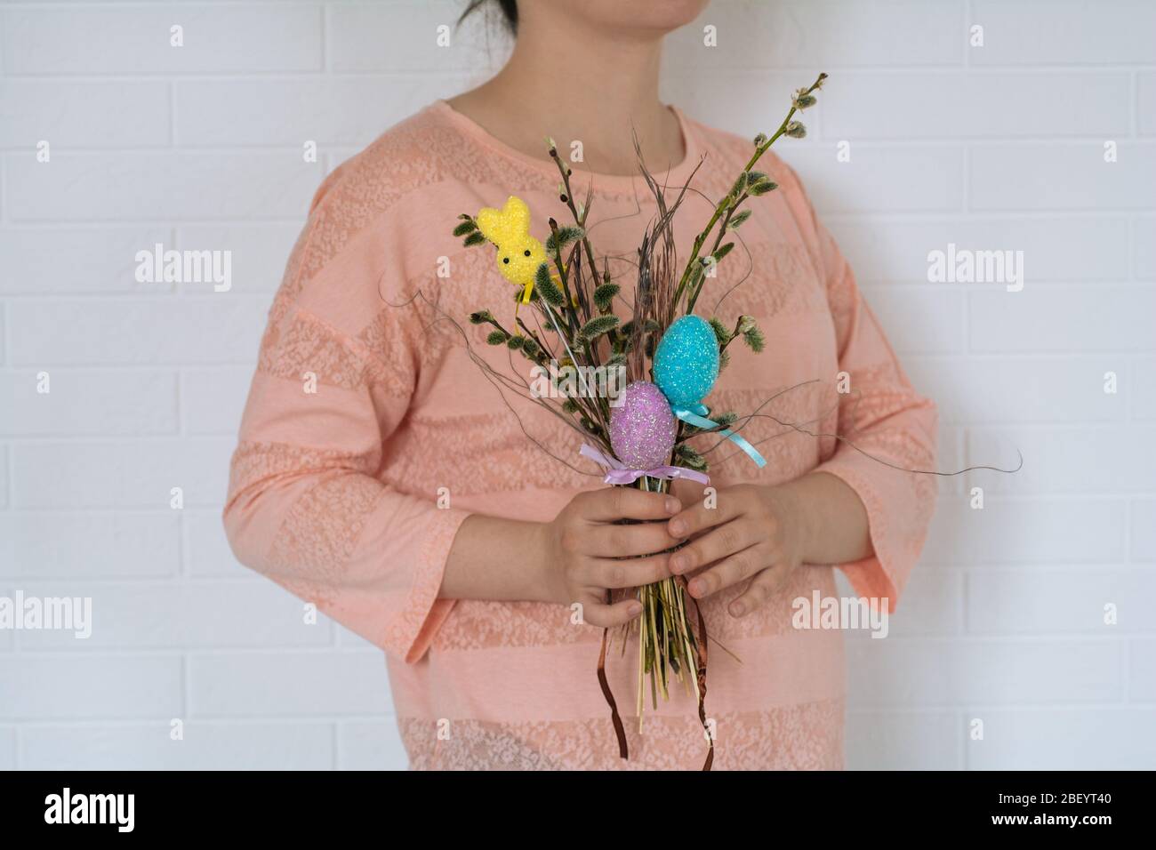 Una giovane ragazza in una t-shirt rosa tiene un bouquet pasquale di rami con uova di pollo e un coniglio sullo sfondo bianco parete. Vista orizzontale Foto Stock