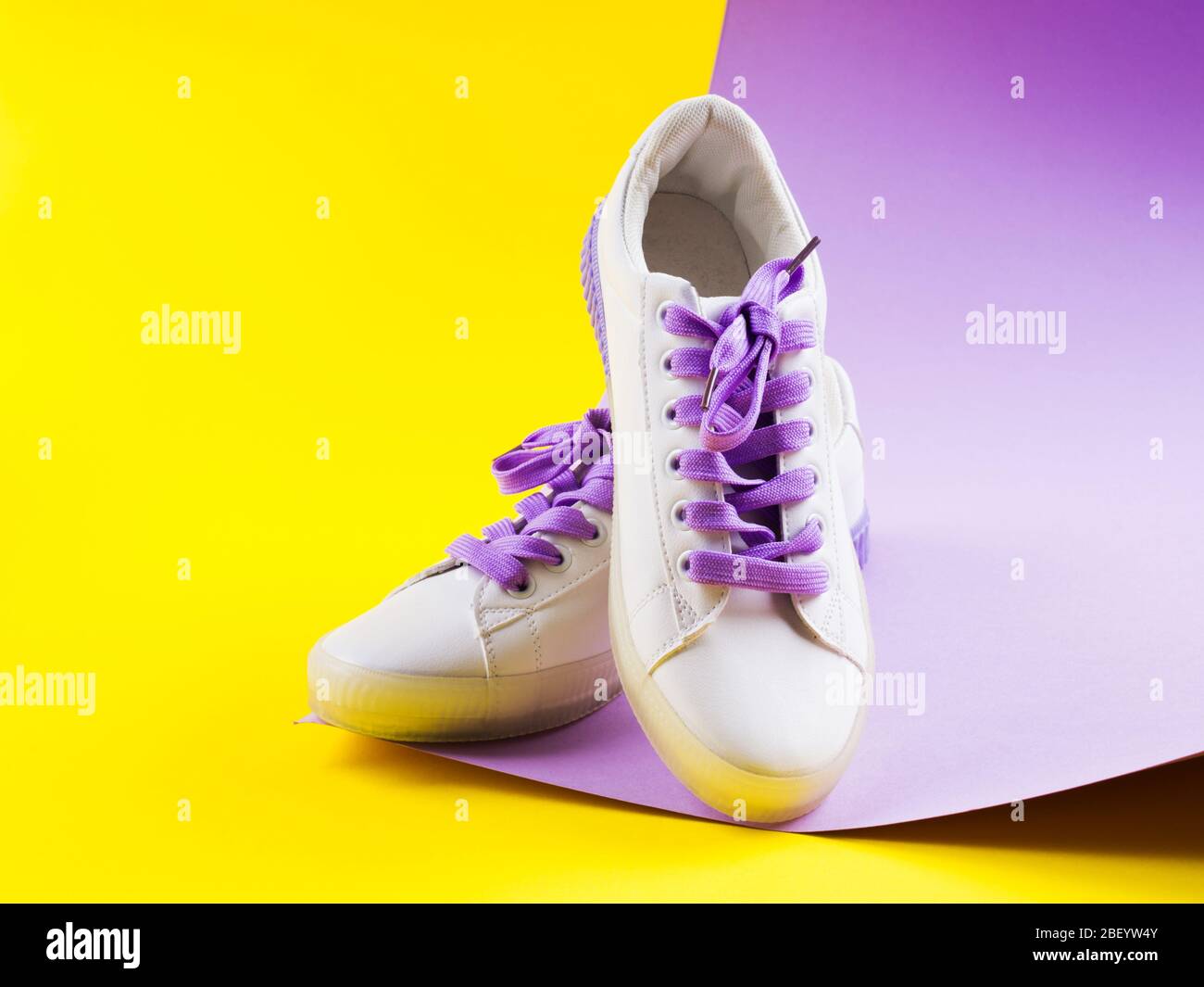 Sneaker bianche con lacci viola su sfondo giallo Foto Stock