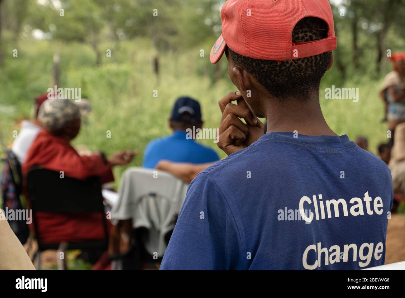 Un giovane uomo Ju/hoansi guarda su di indossare una t-shirt che indica una delle più grandi minacce al suo modo di vivere. Foto Stock