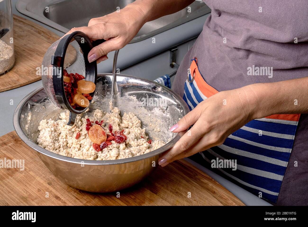 Mani della donna che mettono frutta secca in farina mentre fanno la pasticceria fatta in casa. Foto Stock