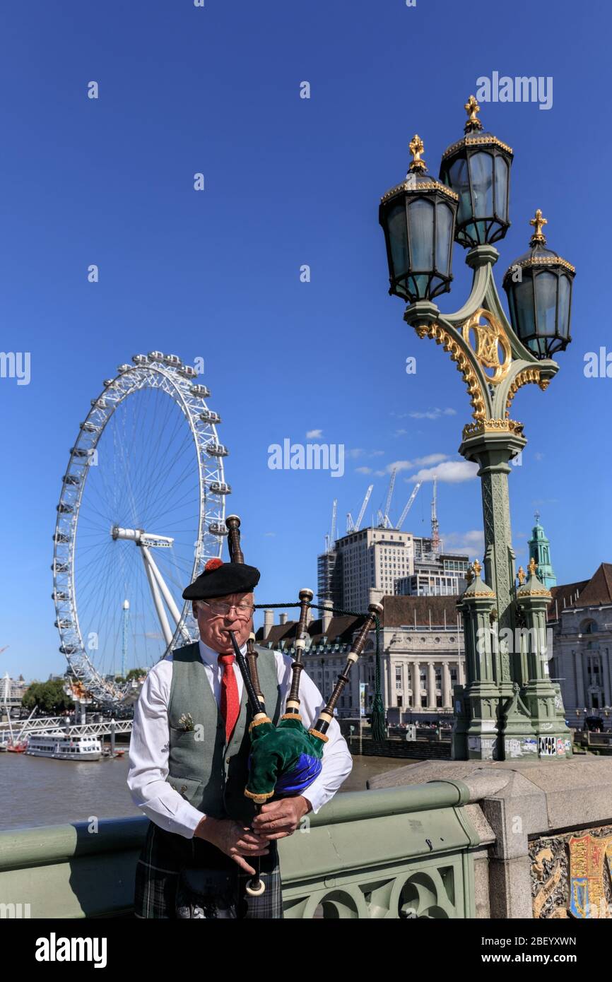 Un piper suona le cornamuse tradizionali sul Westminster Bridge con il London Eye sullo sfondo, Londra, Regno Unito Foto Stock