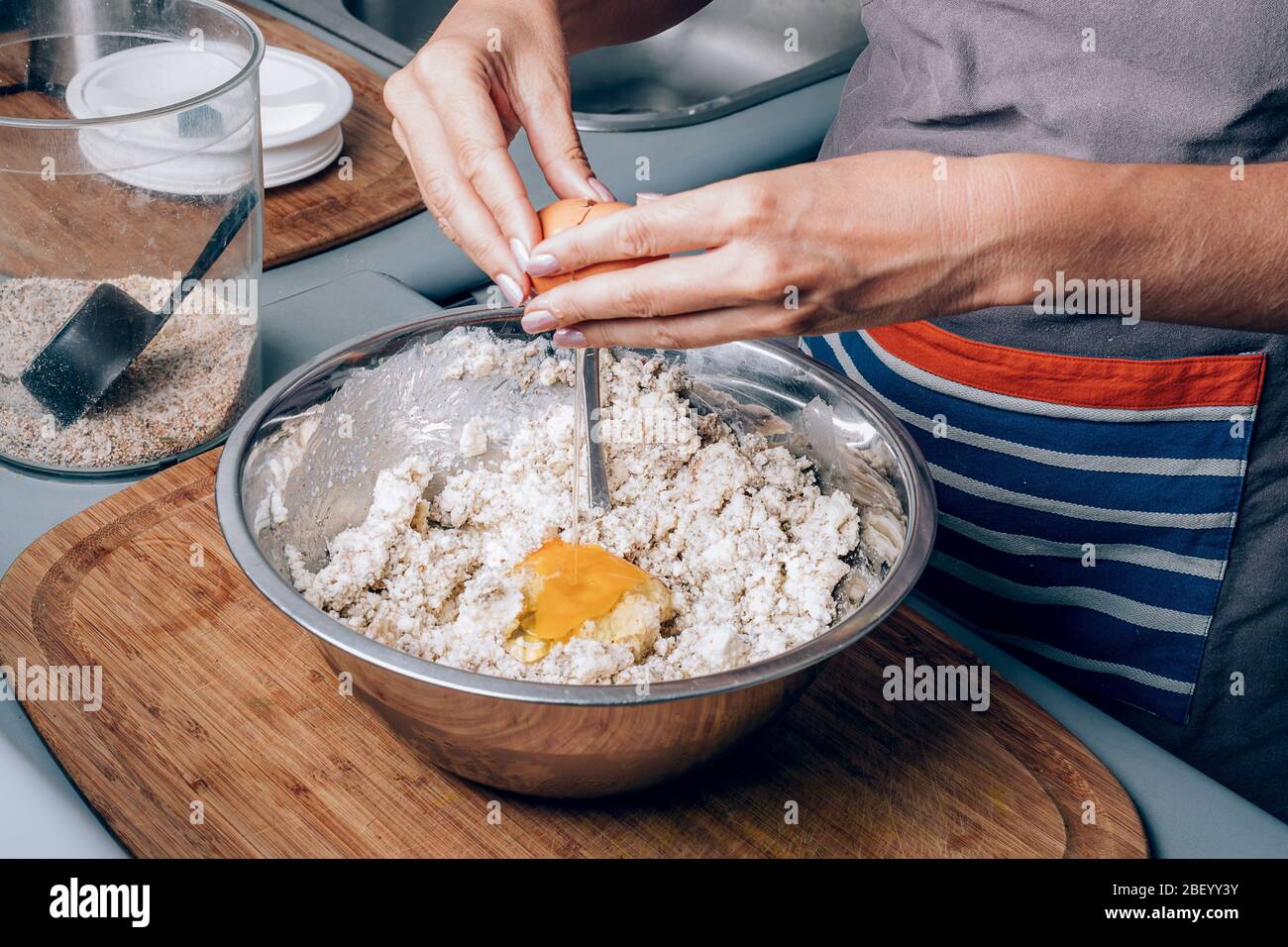 Le mani della donna schiacciano un uovo e lo mettono in farina mentre fanno la pasticceria fatta in casa. Foto Stock