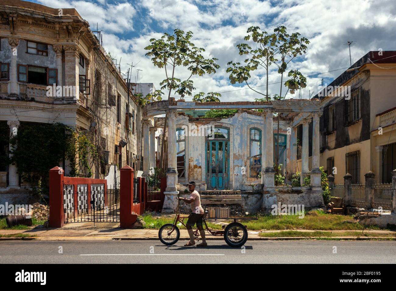 Uomo che spinge un trike di consegna oltre le rovine di vecchi edifici coloniali l'Avana con un segno in spagnolo che dice non cucciolare, Calle 17, l'Avana Cuba Foto Stock