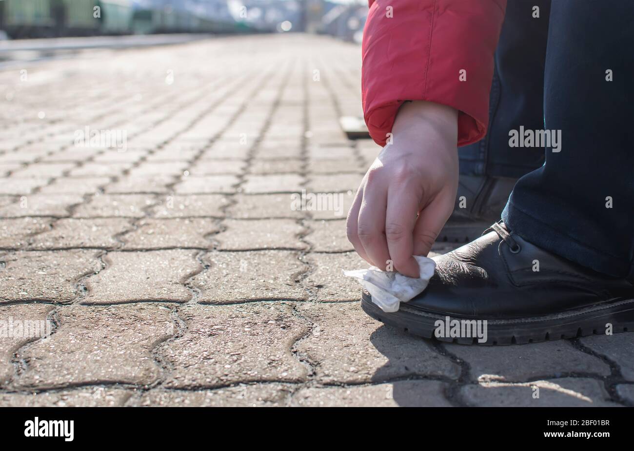 un uomo pulisce scarpe, stivali con un panno umido, un panno, mentre sulla piattaforma di una stazione ferroviaria Foto Stock