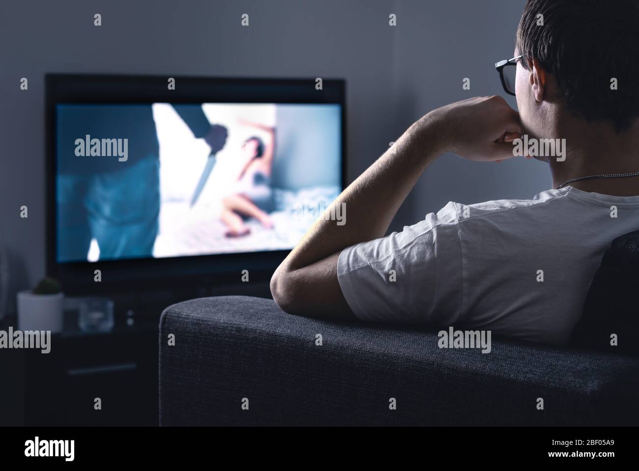 Film horror in streaming sulla tv. Uomo che guarda film o serie spaventosi in streaming online o servizio VOD in un salotto di casa oscuro di notte. Foto Stock