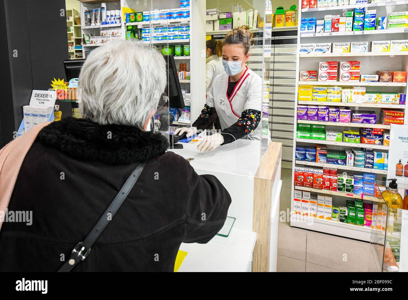 Rouen (Francia settentrionale), epidemia di coronavirus e quarantena il 3 aprile 2020: Schermi in plexiglass installati in una farmacia. Farmacista che indossa una maschera h Foto Stock