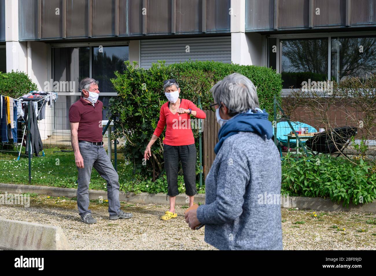 La Rochelle (Francia occidentale) il 7 aprile 2020, scoppio di coronavirus e quarantena: Tre persone con maschere che parlano insieme in fondo ad un'edificazione Foto Stock